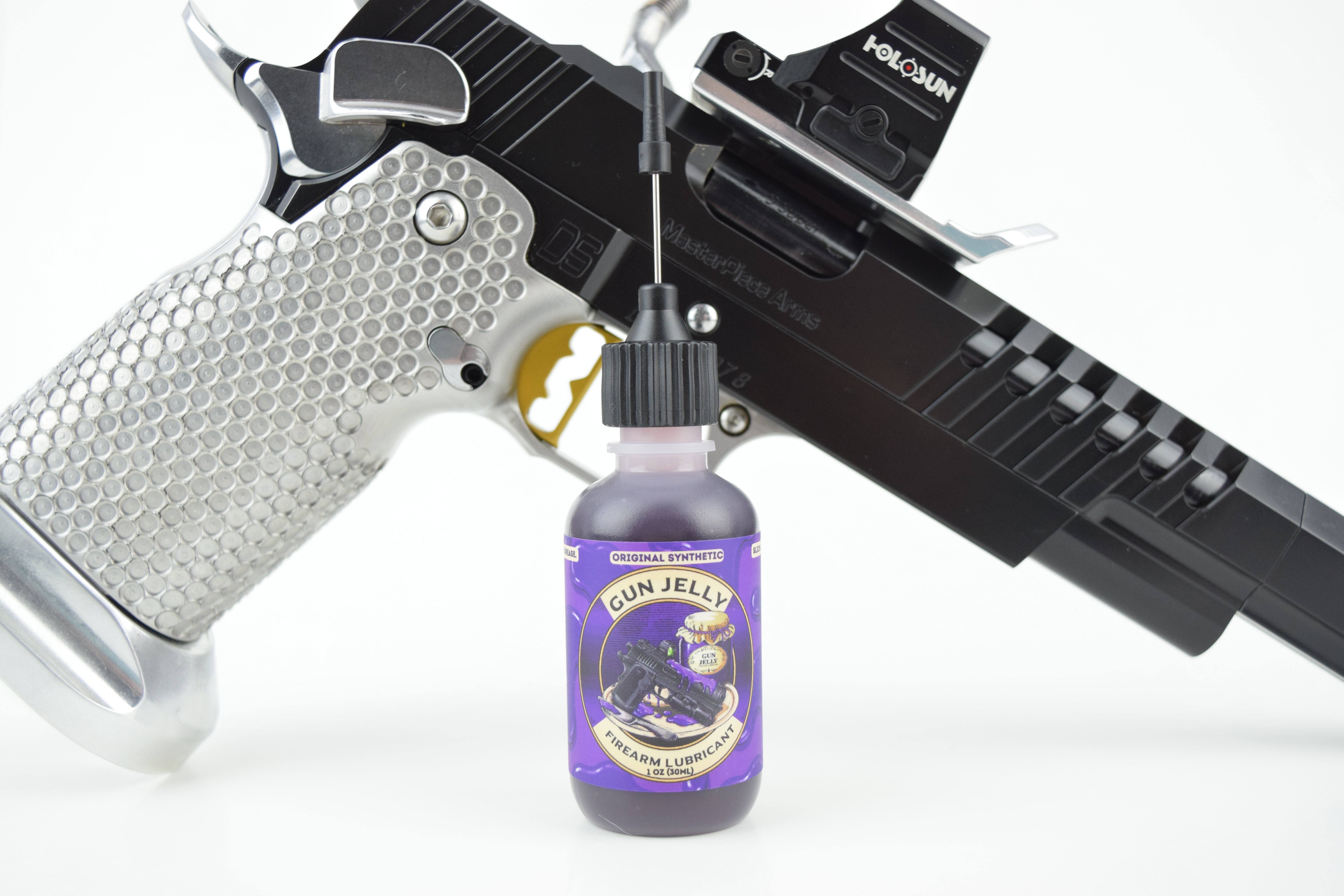 A small bottle labeled 'Gun Jelly' with a purple label and dropper cap, placed in front of a black and silver handgun on a white background.